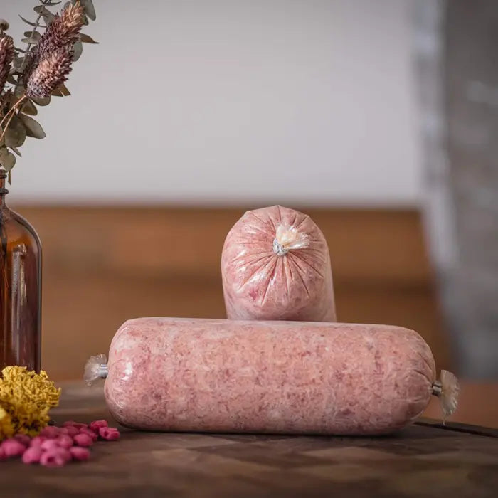 Two large raw dog food tubes of turkey on a wooden surface with a blurred background